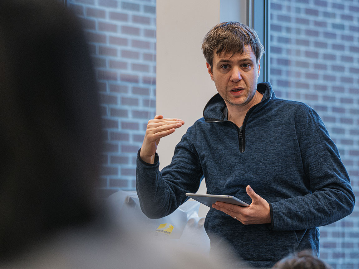 A college professor in a blue shirt gestures while teaching class